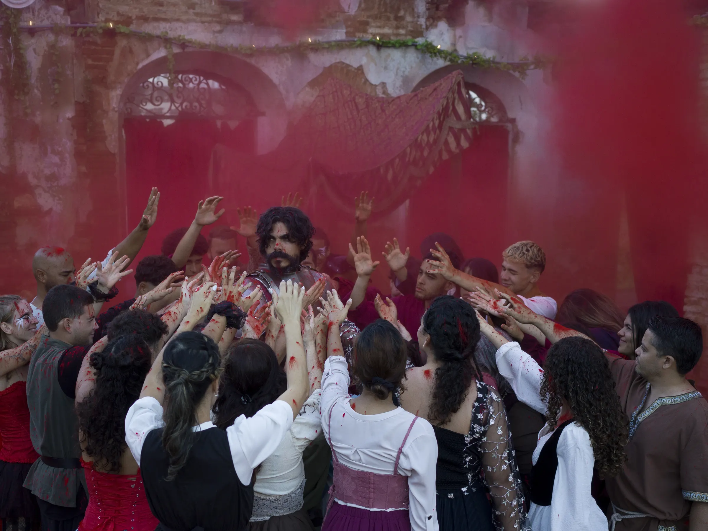 A crowd of villagers reach toward a lone figure through red smoke