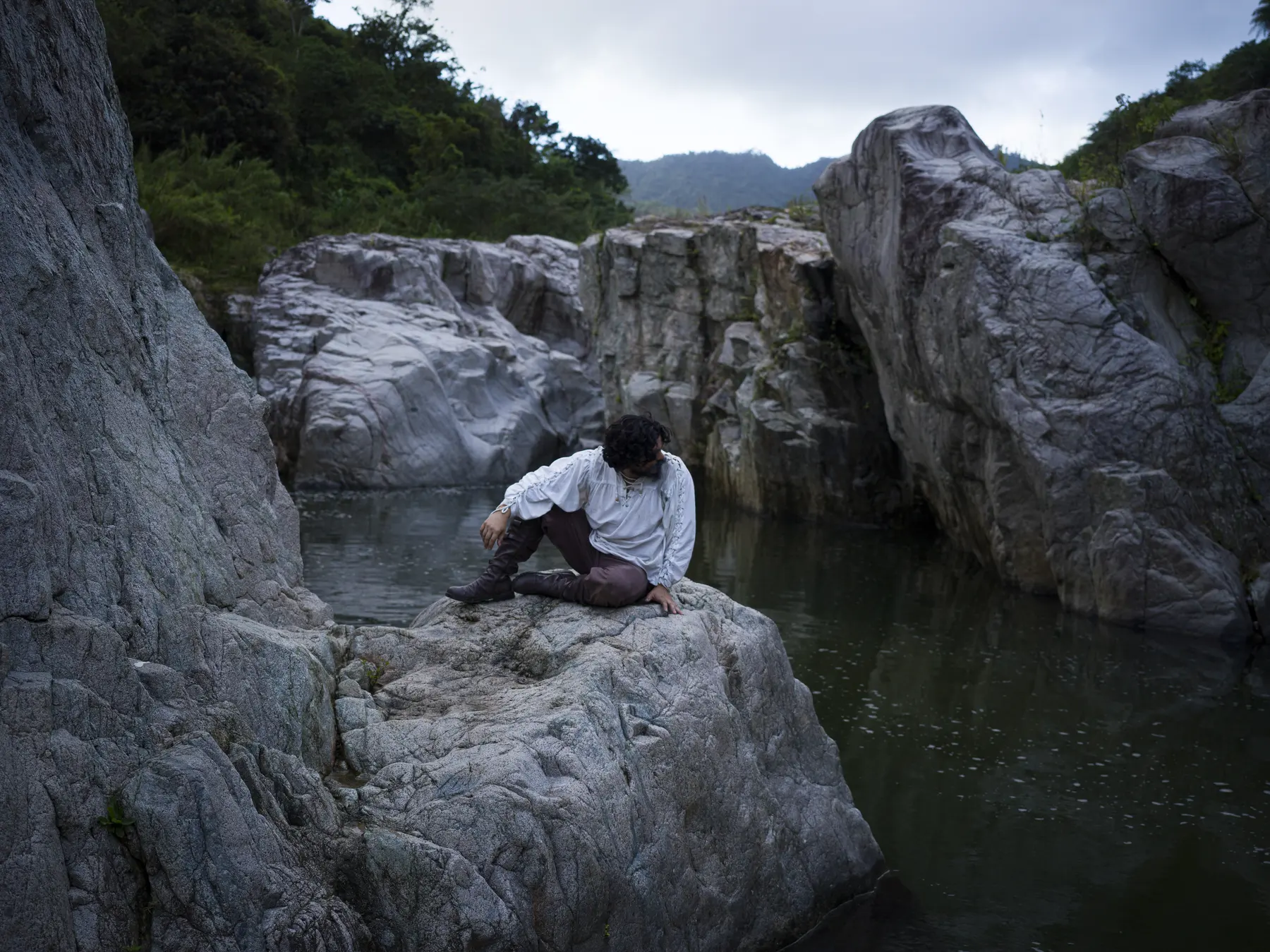 A lone figure seated on rocks in a river gorge