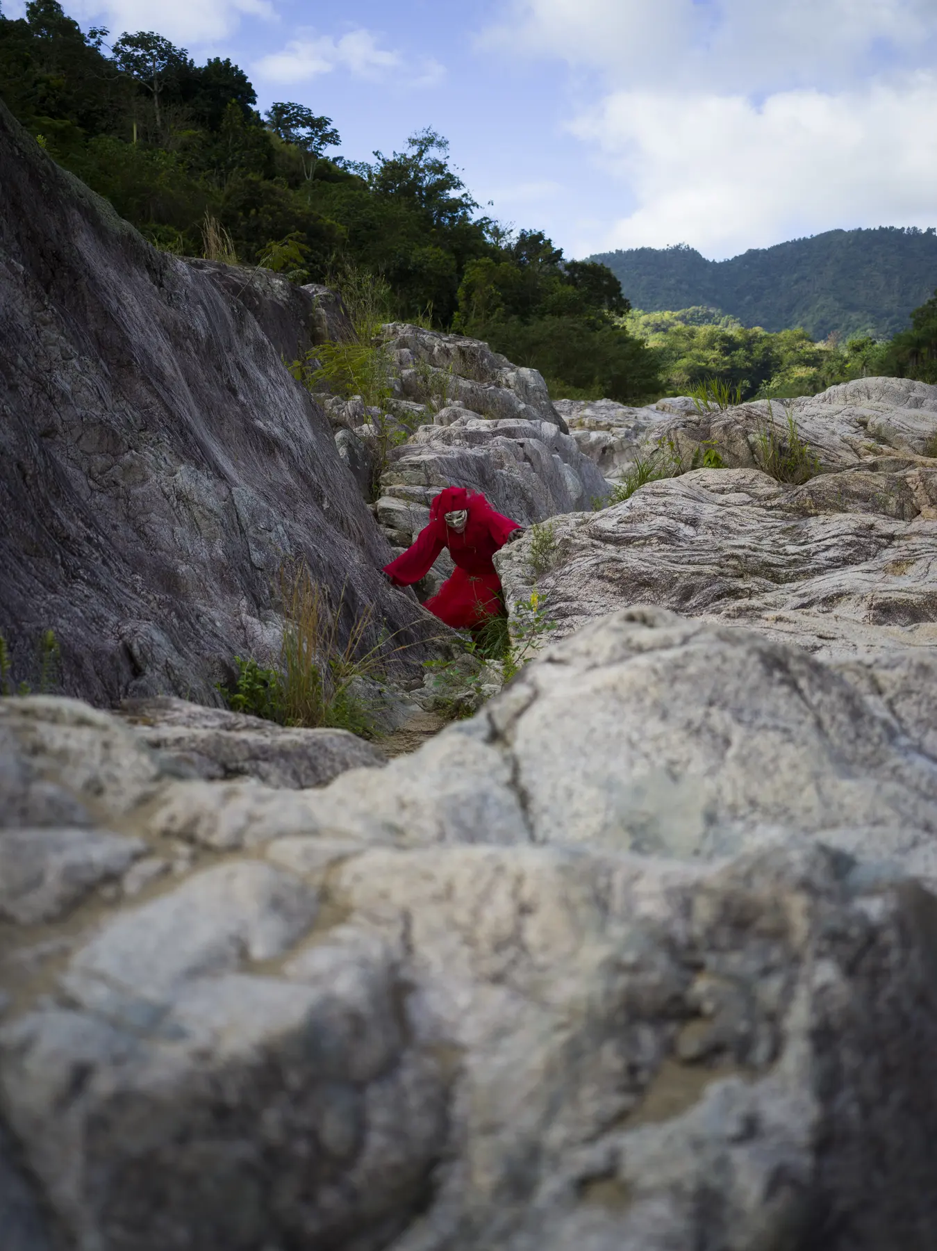 A red-clad figure crossing pale limestone above the river