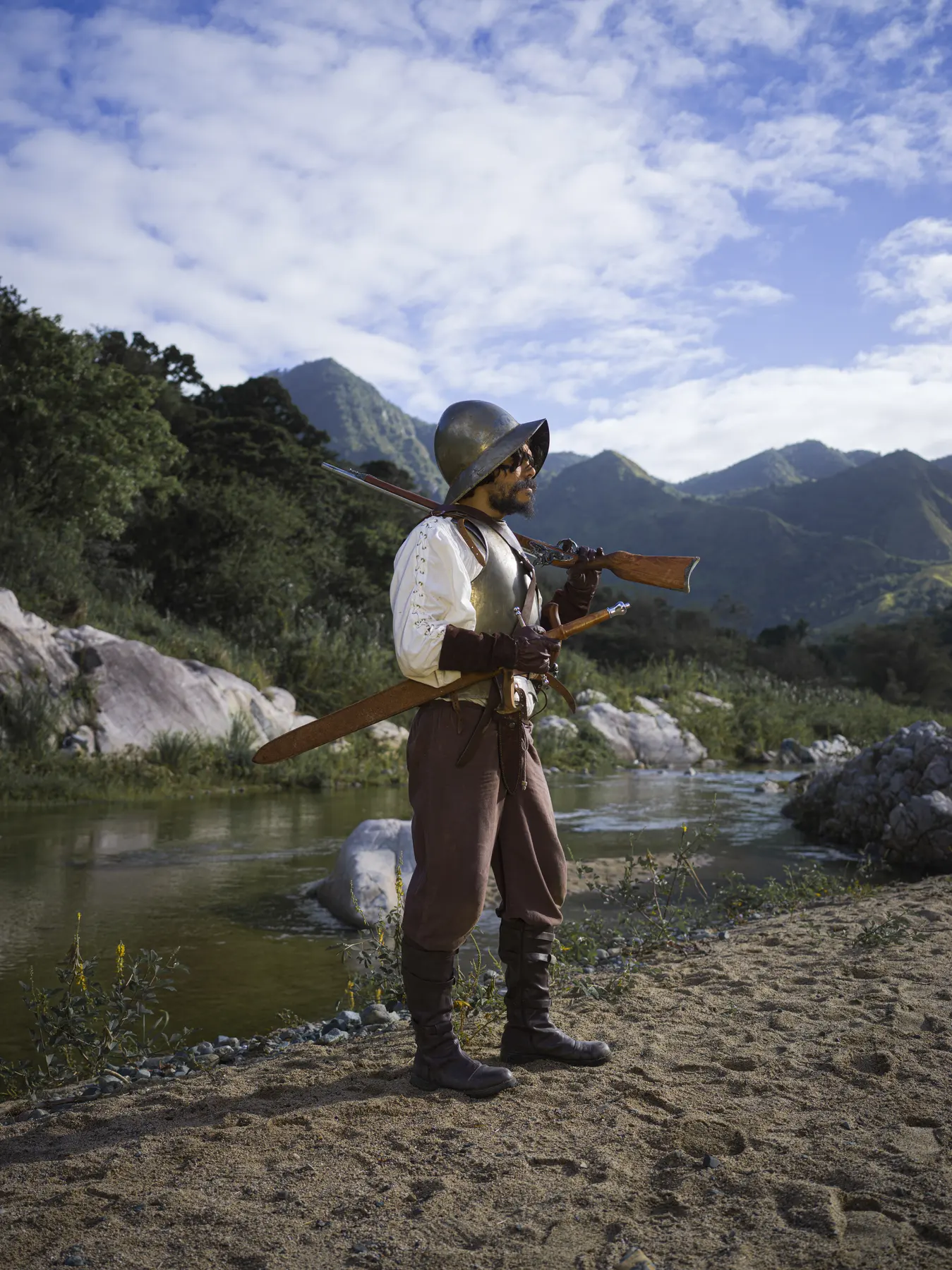 A soldier with a matchlock stands in the riverbed