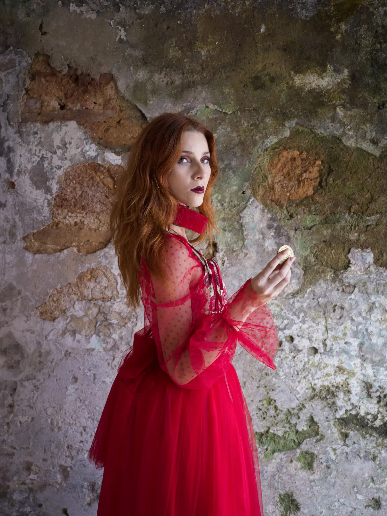 A woman in a red gown against a weathered plaster wall