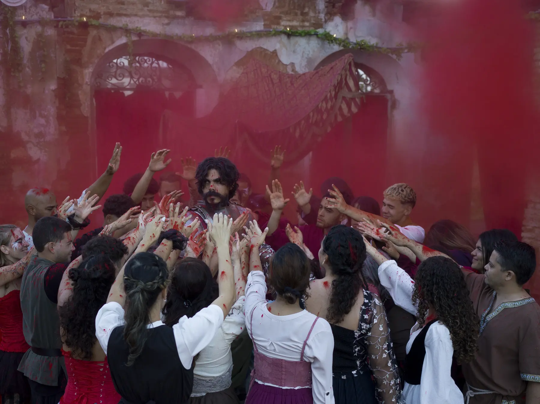 A crowd raises bloodied hands toward a figure in red smoke